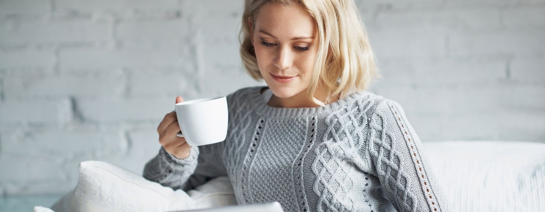 a person sitting down holding a cup looking at a tablet
