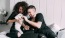 a man and woman sitting on a bed playing with a dog