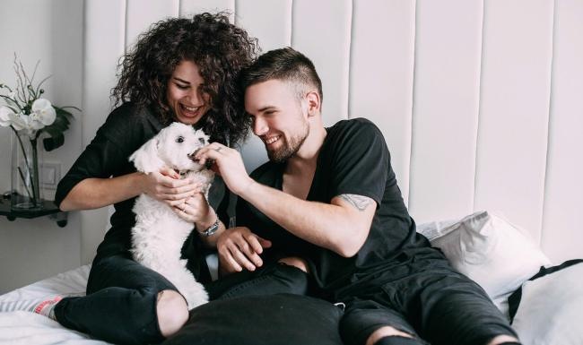 a man and woman sitting on a bed playing with a dog